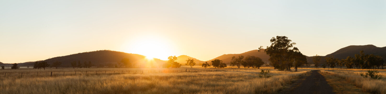 Sun rising up over paddock and dirt road on farm