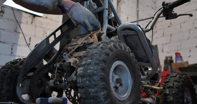 Installing a new part on an ATV to replace a broken old one. Do-it-yourself repair of a children's ATV in the garage for a child. A father is repairing his son's ATV in the garage.