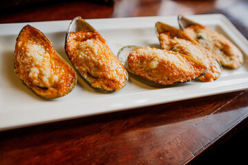 Baked mussels with sauce and cheese on a white plate