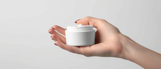 Fototapeta na wymiar Hand gracefully holding an open jar of cream on a clear, minimalistic background.