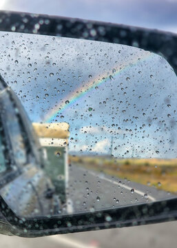 Raindrops on side mirror of car with view of caravan and rainbow