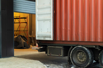 A large red container truck is parked in a loading dock