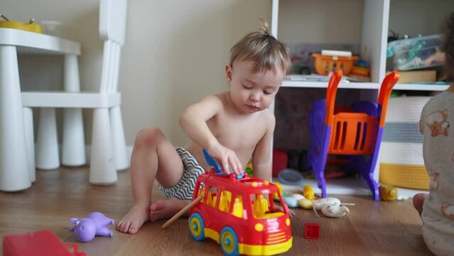 baby child playing toy car on the floor in kindergarten. happy family kid concept. baby son playing red bus toy indoors. child boy blond plays with a toy lifestyle car in kindergarten