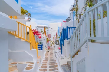 Fotobehang narrow side street with traditional whitewashed walls and blue accents in Mykanos Greece. traditional windmill on the sea shore and colorful restaurants © Birol