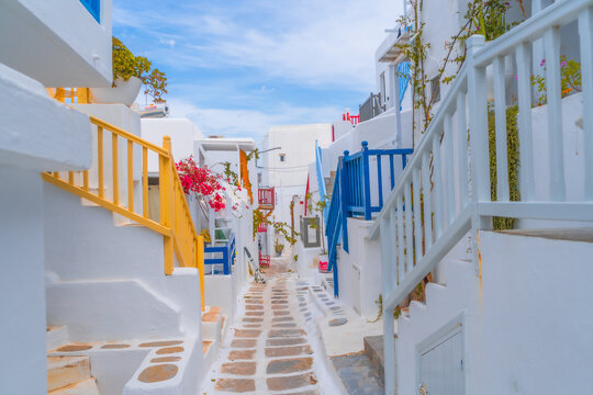 Fototapeta narrow side street with traditional whitewashed walls and blue accents in Mykanos Greece. traditional windmill on the sea shore and colorful restaurants