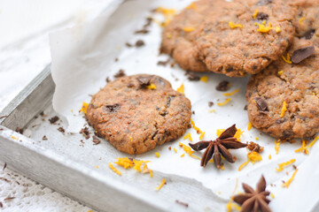 home made chocolate cookies with orange zest, chocolate chips and spices perfect for christmas on grey wooden background close up selective focus