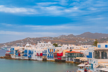 narrow side street with traditional whitewashed walls and blue accents in Mykanos Greece. traditional windmill on the sea shore and colorful restaurants