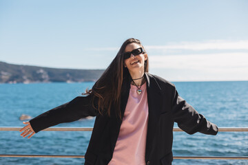 Smiling smart woman tourist walking outdoors. Woman wear black sunglasses and black jacket. Happy...