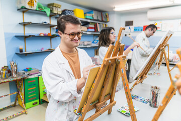 Man with Down syndrome paints with focus in an inclusive art class.