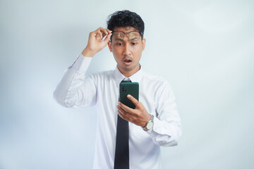 Adult Asian man looking to mobile phone that he hold with surprised expression
