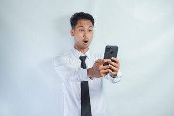 Adult Asian man looking to mobile phone that he hold with surprised expression