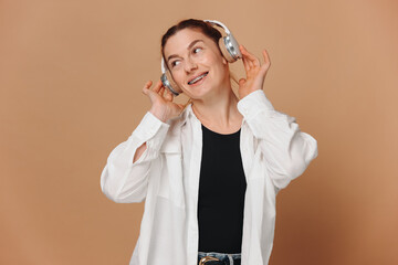 Modern woman smiling with braces on her teeth and listening to music in headphones on a beige background