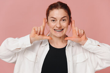 Modern happy woman showing braces on pink background, orthodontics concept