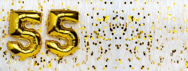 Golden foil balloon number, figure fifty-five on white with confetti background. 55th birthday...