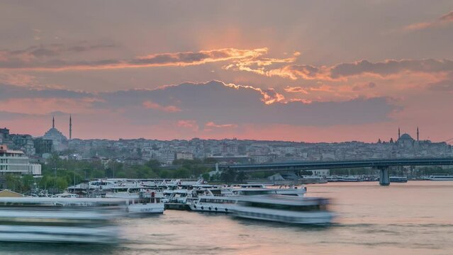 Many passenger ferrys near boat station in the Bosphorus and Golden Horn at sunset timelapse, Istanbul skyline, Turkey. Mosque and bridge on background with reflection on water at sping evening