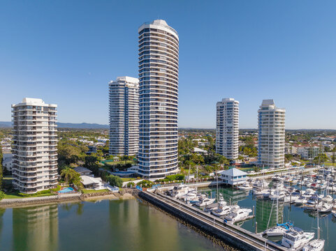 Aerial view of high rise apartment towers and boat marina along a waterfront esplanade