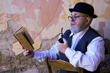 Man with beard pipe hat and vintage clothes reading a book