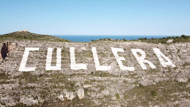 Aerial view approaching the big sign of Cullera, painted on the slope of the Sierra de los Zorros next to the town of Cullera in the province of Valencia (Spain)