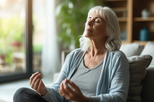 Peaceful senior woman doing breathing exercise at home, mature woman meditating at home with eyes closed