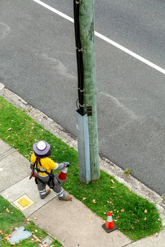An electric power line worker stands at base of wooden power pole.