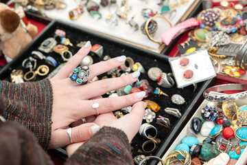 Girl picks out and tries on old used precious rings and studs at a flea market. Girl's hand with...