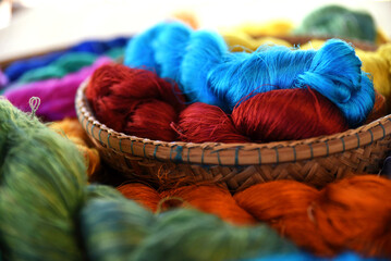 Tie of colorful and shiny beautiful silk yarn dyed placed in a pile of round bamboo baskets. Prepared for use as a raw material for weaving silk. - obrazy, fototapety, plakaty