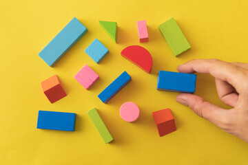 Colorful wooden toy blocks on yellow background and human hand