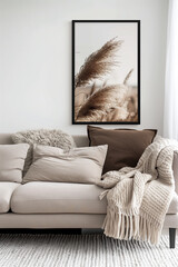Beige sofa with pillows and blanket against white wall with framed poster mockup, in a minimalistic style, for living room decor, with natural light, soft tones, and pampas grass in the background