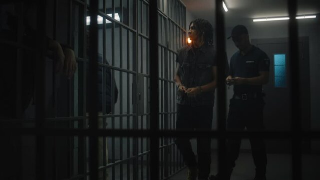 Warden brings new prisoner in jail cell and takes off his handcuffs. African American teenager serves imprisonment term in jail. Young inmates in prison cells. Justice system. View through metal bars.
