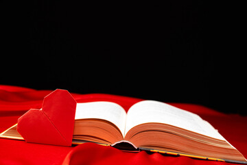 Origami paper heart and thick book on red and black background. Love for books.