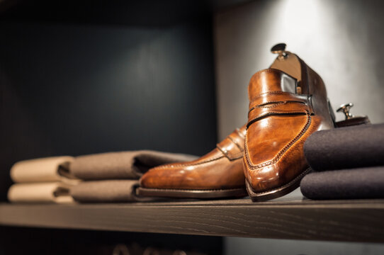 Shelf with brown handmade shoes and few folded sweater pullovers. Wardrobe with man costumes. Closet in apparel boutique. Dark brown furniture.