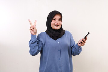 Wow excited asian adult woman standing holding a cell phone while showing two fingers