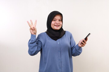 Wow excited asian adult woman standing holding a cell phone while showing three fingers