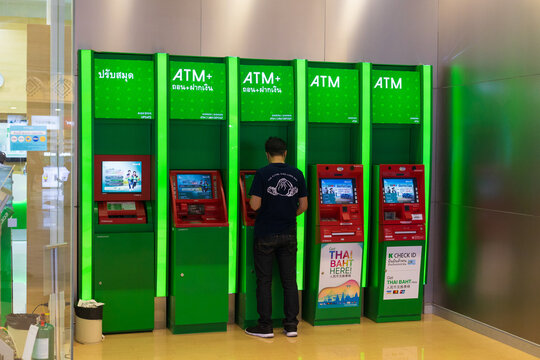 Pattaya, Thailand - 23 December, 2023: unrecognizable man withdraws cash from green ATM. Man using cash machine a Thai bank. A row of Automated teller machine or ATM line the wall indoors