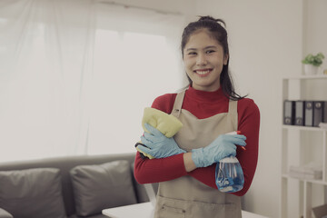 Asian woman doing housework wearing an apron cleaning the wooden floor in the living room Happy housewife doing housework at home with attractive smile, house cleaning concept