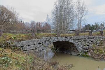 Fototapeta na wymiar Old stone arch bridge over Vähäjoki river in cloudy autumn weather, Mallusjoki, Finland.