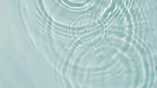 transparent blue slow motion water wave circles with rain drops from above, sunny pure water texture background for beauty care, spa and cosmetics