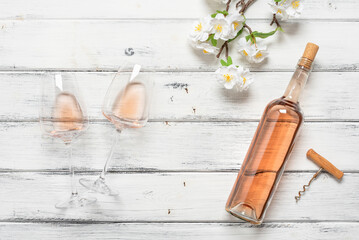 Rose wine in a bottle and glasses flat lay on a white wooden background decorated with a blossoming cherry branch. Top view. Spring wine tasting.
