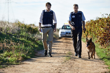 Detective, dog and walk in field for robbery or crime scene with car for search, safety and law enforcement. Policeman, investigation and uniform in outdoor working at countryside with gravel road