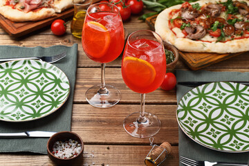 Two glasses of Aperol spritz cocktail on wooden table, served with tableware and pizza