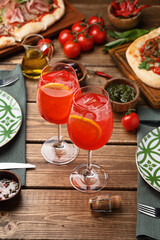 Two glasses of Aperol spritz cocktail on wooden table, served with tableware and pizza