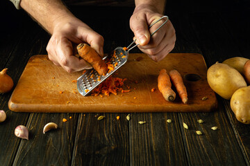 Close-up of a chef hands grating carrots to prepare a vegetarian dish. Concept of cooking...
