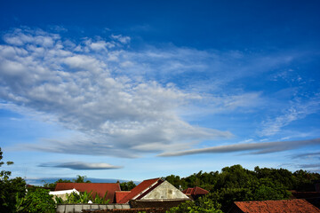 Fototapeta na wymiar Beautiful cloudy blue morning sky with houses roof foreground at bottom