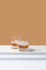 Dos vasos de whisky con hielo sobre un fondo naranja