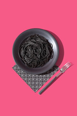 Espaguetis con tinta de calamar negro en un plato con tenedor sobre fondo rosa. Vista superior