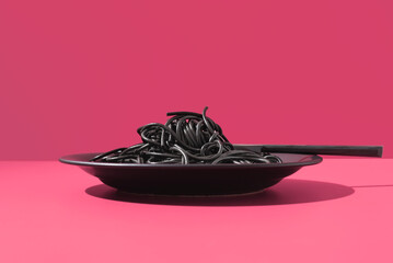 Espaguetis con tinta de calamar negro en un plato con tenedor sobre fondo rosa - obrazy, fototapety, plakaty