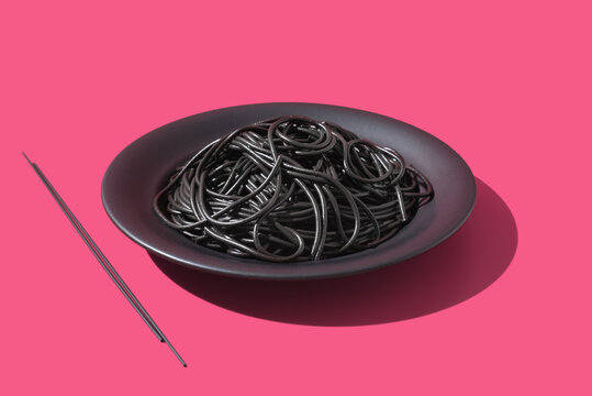 Espaguetis con tinta de calamar negro en un plato sobre fondo rosa