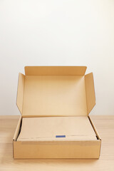 Open cardboard box with item wrapped in kraft paper on wooden table. Delivery service