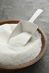 Granulated sugar in bowl and scoop on grey textured table, closeup