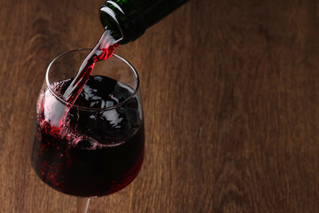 Pouring tasty red wine in glass at wooden table, closeup. Space for text